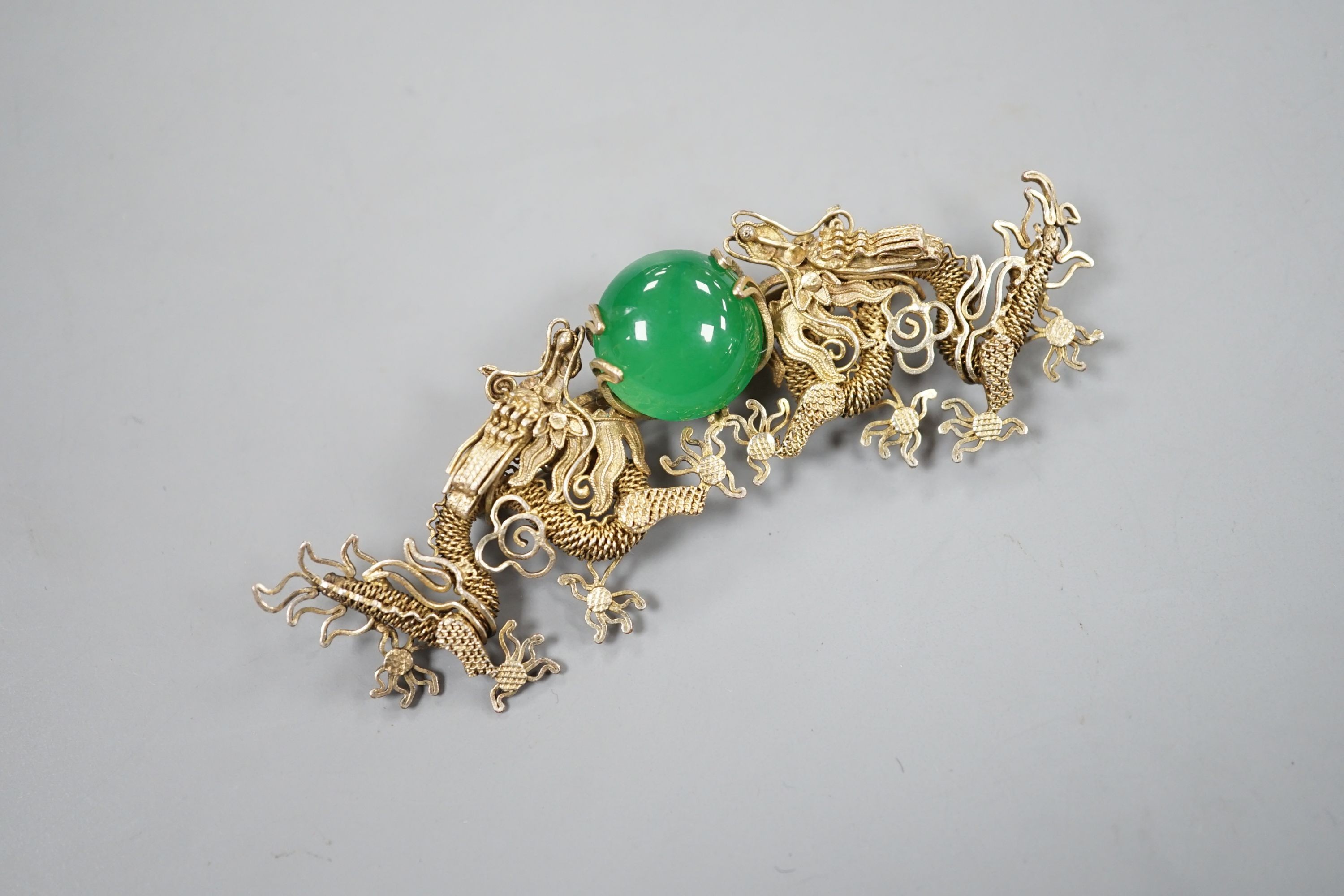 A Chinese gilt white metal and green cabochon stone set filigree dragon brooch, 88mm.